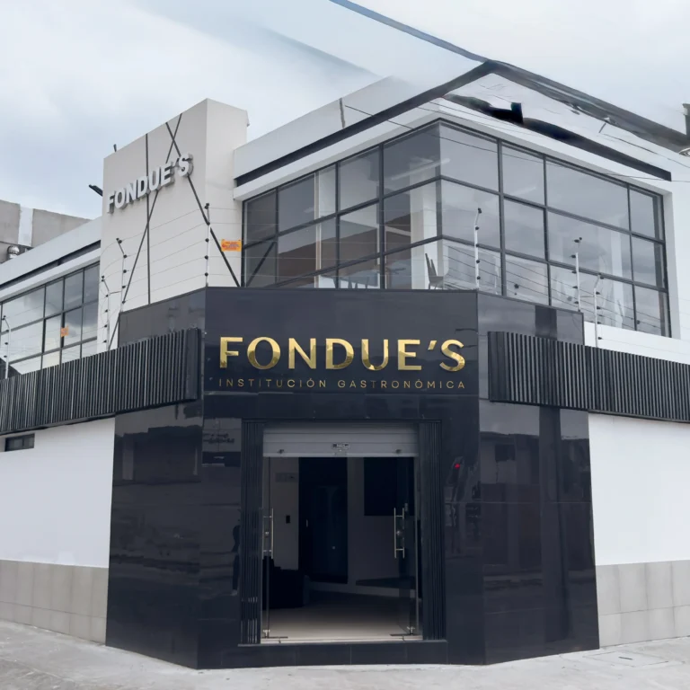 Fachada exterior del edificio moderno de Fondue's Institución Gastronómica, con acabados en negro brillante, letras doradas y amplios ventanales.
